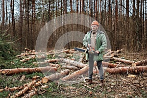 Logging, Worker in a protective suit with a chainsaw. Cutting down trees, forest destruction. The concept of industrial
