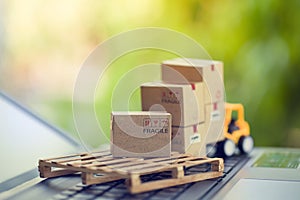 Logistic and cargo freight concept: Fork-lift a truck moves a paper box on notebook keyboard in the natural green background.