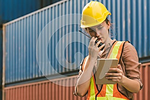 The logistics female staff is standing in front of colorful containers at habour warehouse and talking on phone. Supply chain and