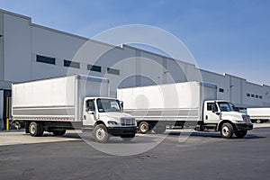 Logistics hub with warehouse building and day cab middle duty semi trucks with box trailers waiting for the next load and local photo