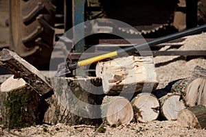 Logs and tractor driven saw with woodcutting axe.