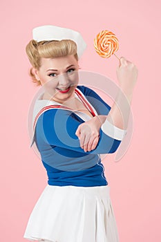 Lollipop can do best concept. Orange big lollipop in hand of attractive blonde female with curls and sailor uniform.
