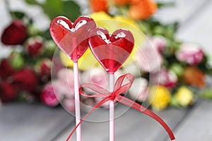 Lollipops in heart shape on background of colorful roses