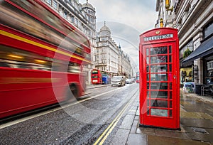 London, England - Iconic blurred vintage red double-decker bus on the move with traditional red telephone box