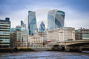 London, England - Iconic red double-decker buses on London Bridge with office buildings and famous skyscrapers at background