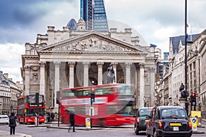 London, England - Iconic red double decker busses on the move and black and green london taxies with the Royal Exchange building