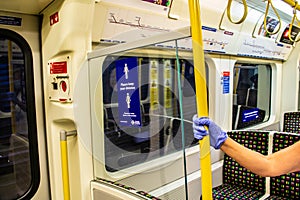 LONDON/ENGLAND- 2 June 2020: Passenger wearing disposable gloves, holding a hand rail on a London Underground tube train