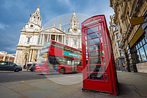 London, England - Traditional red telephone box with iconic red double-decker bus on the move at St.Paul`s Cathedral