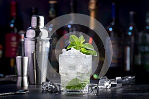 London Mint Swizzle alcohol cocktail drink with dry gin, lemon juice, sugar syrup, soda, mint and ice. Black bar counter