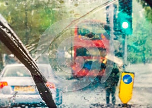 London street scene abstracted by rain on a car windscreen on a rainy day. A red bus can be seen and a man holding cardboard above