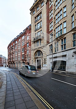 London taxi moving down a wet street without people surrounded by buildings photo