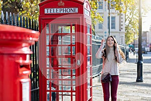 London traveler woman stands next to a red telephone booth and talking to her phone
