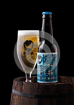 LONDON, UK - FEBRUARY 06, 2019: Bottle and glass of Punk IPA beer, from the Brewdog brewery on old wooden barrel on black