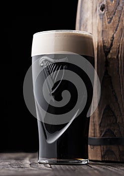 LONDON, UK - MAY 03, 2018: Original glass of Guinness draught stout beer next to wooden barrel on dark wooden background.