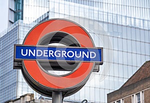 London Underground tube station sign with office buildings in background.