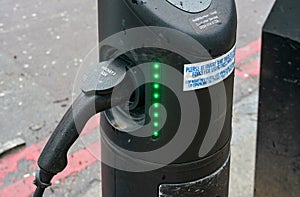 London, United Kingdom - February 04, 2019: Electric vehicle charging socket on public street, cable plugged in with lights on,