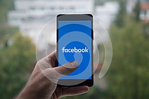 Man holding smartphone with Facebook logo with the finger on the screen