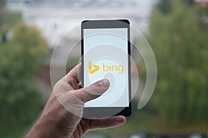 Man holding smartphone with Microsoft Bing logo with the finger on the screen