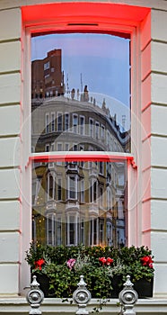 London - Yellow building with bay windows reflected in a window across the street with dramatic red lighting on sills and a window