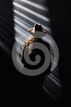 A lone blonde woman in the dark wearing a coat and a hat, seen from behind.