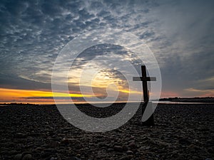 A Lone Cross On A Rocky Beach At Sunrise