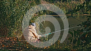 Lone Elderly Fisherman Sitting on the River Bank with a Fishing Rod Catches Fish