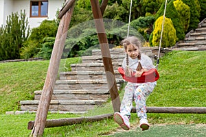Lone elementary school age child, young girl having fun playing around swinging on an outdoors swing on the playground