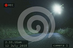 A lone figure standing in the road at night while looking at a UFO and beam of light in the sky. With a CCTV edit.