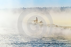 A lone fisherman on the misty lake with a fishing rod, early in the morning
