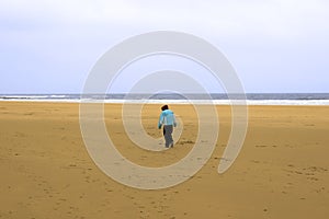 Lone girl walking a beach against the cold wind