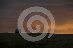 Lone hay pile stands on a grass field hill