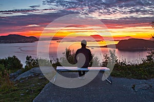 A Lone Man Sitting on A Bench Overlooking Islands and Ocean at Dramatic Sunset