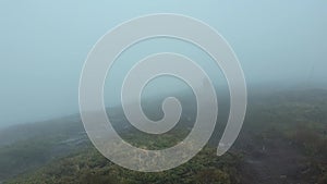 Lone man wanderer walking a hilly road as climbing a mountain in a cold windy day as the wind is blowing clouds and the mist is mo