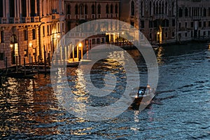 Lone motorboat floats the Grand Canal in Venice in glowing lights against the backdrop of blue water on a summer evening