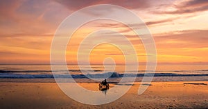 A lone motorcycle and rider driving along a beach at sunset