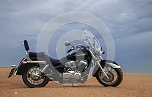 Off-road motorcycle standing still in the open desert beneath heavy clouds