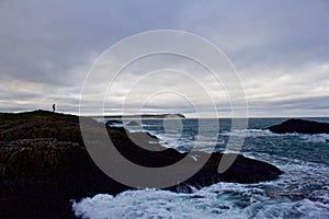 Lone person overlooks ocean from hill above with turbulent seas below