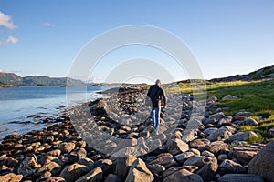 Lone person waling on the rocky rugged shoreline   in a green landscape