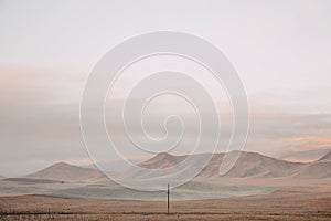 Lone pole in a field on a background of mountains. Dawn in autumn field. Hills in morning haze. Grass covered with autumn