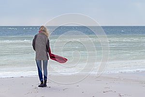 Lone sad beautiful girl walking along the shore of the frozen sea on a cold day, rubella, chicken with a red scarf on the neck photo