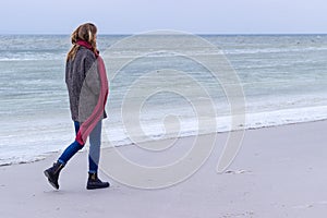 Lone sad beautiful girl walking along the shore of the frozen sea on a cold day, rubella, chicken with a red scarf on the neck photo