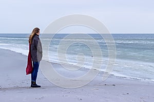 Lone sad beautiful girl walking along the shore of the frozen sea on a cold day, rubella, chicken with a red scarf on the neck photo