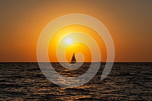 A lone sailboat at sunset. Atmospheric seascape with orange sun