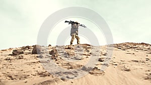 Lone soldier trudging up a sandy slope with carried weapon