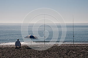 Lone surf fisherman and parasol at beach