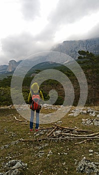 A lone traveller stands on the hill and looks at the mountains. Cloudy dark weather.