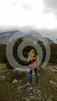 A lone traveller stands on the hill and looks at the mountains. Cloudy dark weather.