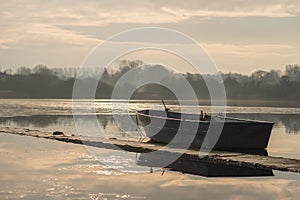 A lone unmanned boat sits idle on a frozen lake during sunrise on Hornsea Mere