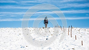 Lone walker climbs on top of white snow ridge. Hillwalking in winter conditions
