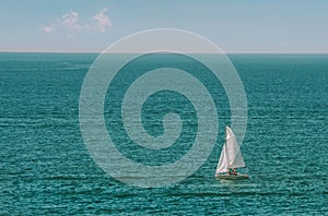A lone white sail sailboat on a calm blue sea